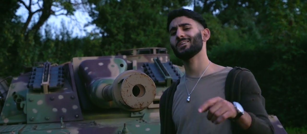 One of the twins singing beside a tank among trees