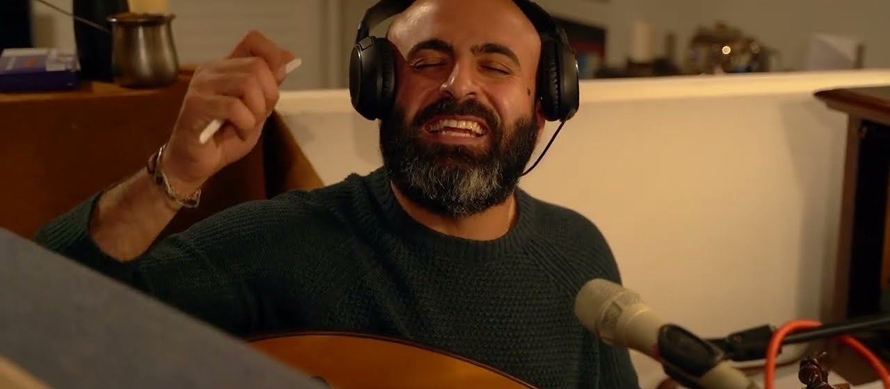 An oud player in headphones laughing mid-take in a warm room