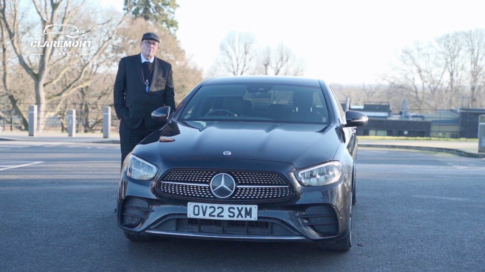 A chauffeur in a dark coat and cap standing beside a black Mercedes