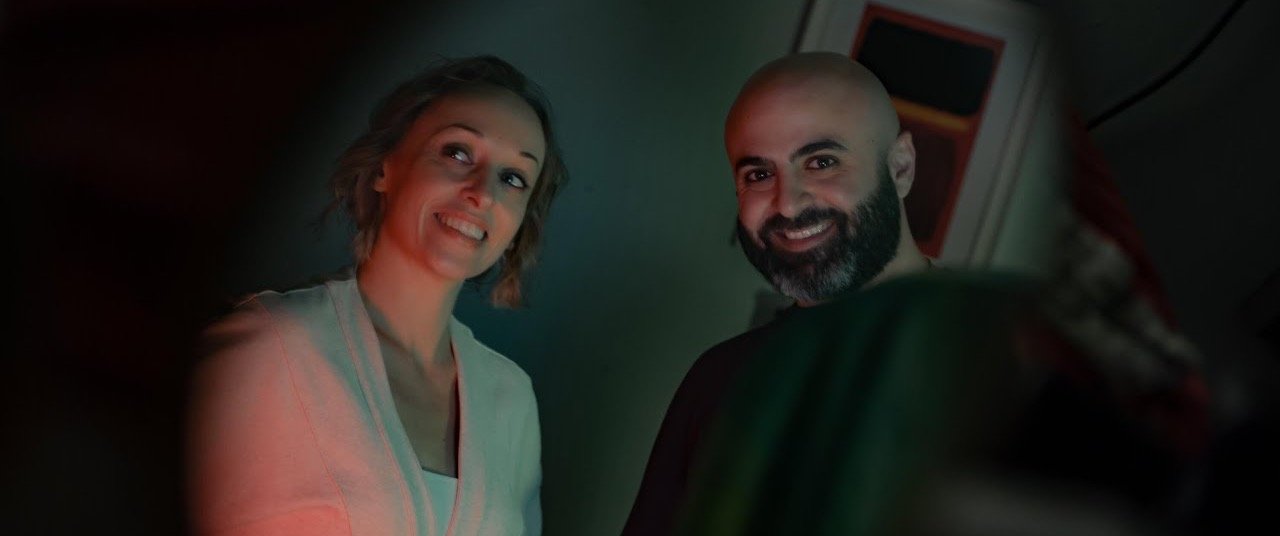 A woman and a man smiling side by side in green and red light