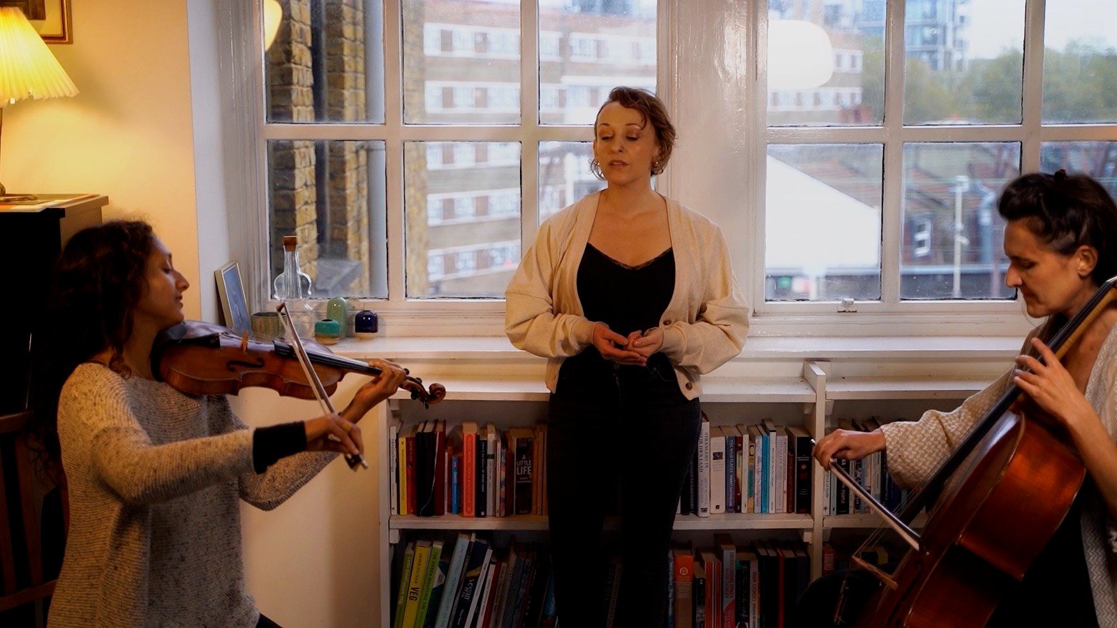 A singer standing at a big window between a violinist and a cellist