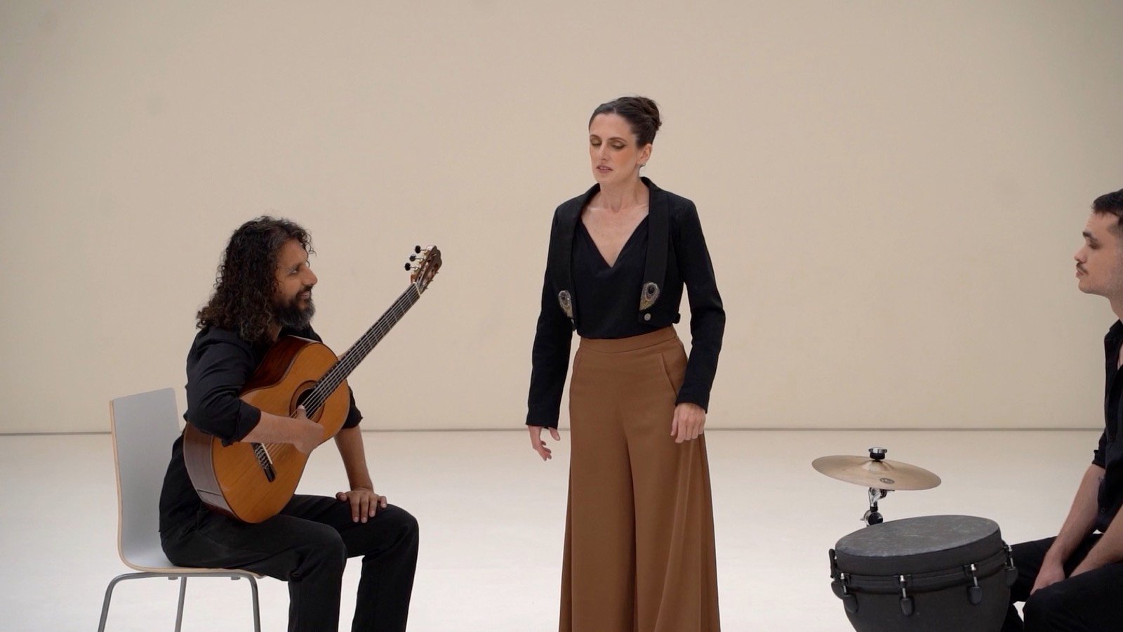 A guitarist, a dancer and a drummer rehearsing in a white studio