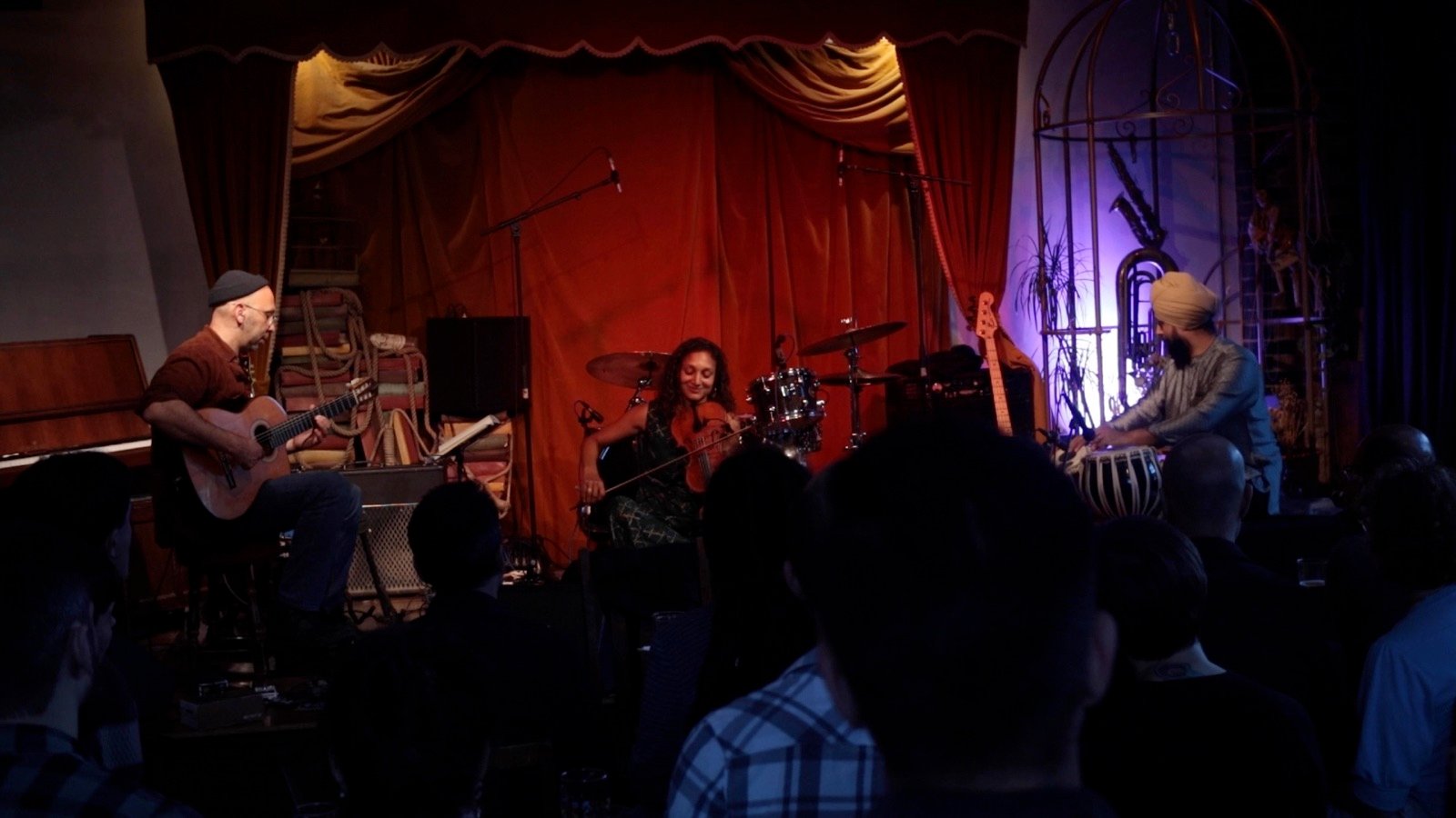 A band on a small club stage in front of a red curtain