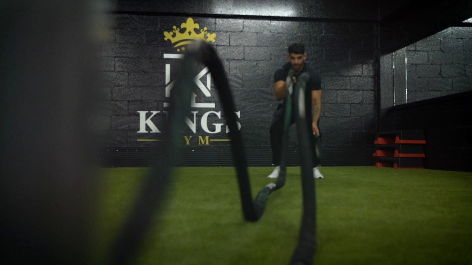 A man working battle ropes in front of the Kings Gym sign