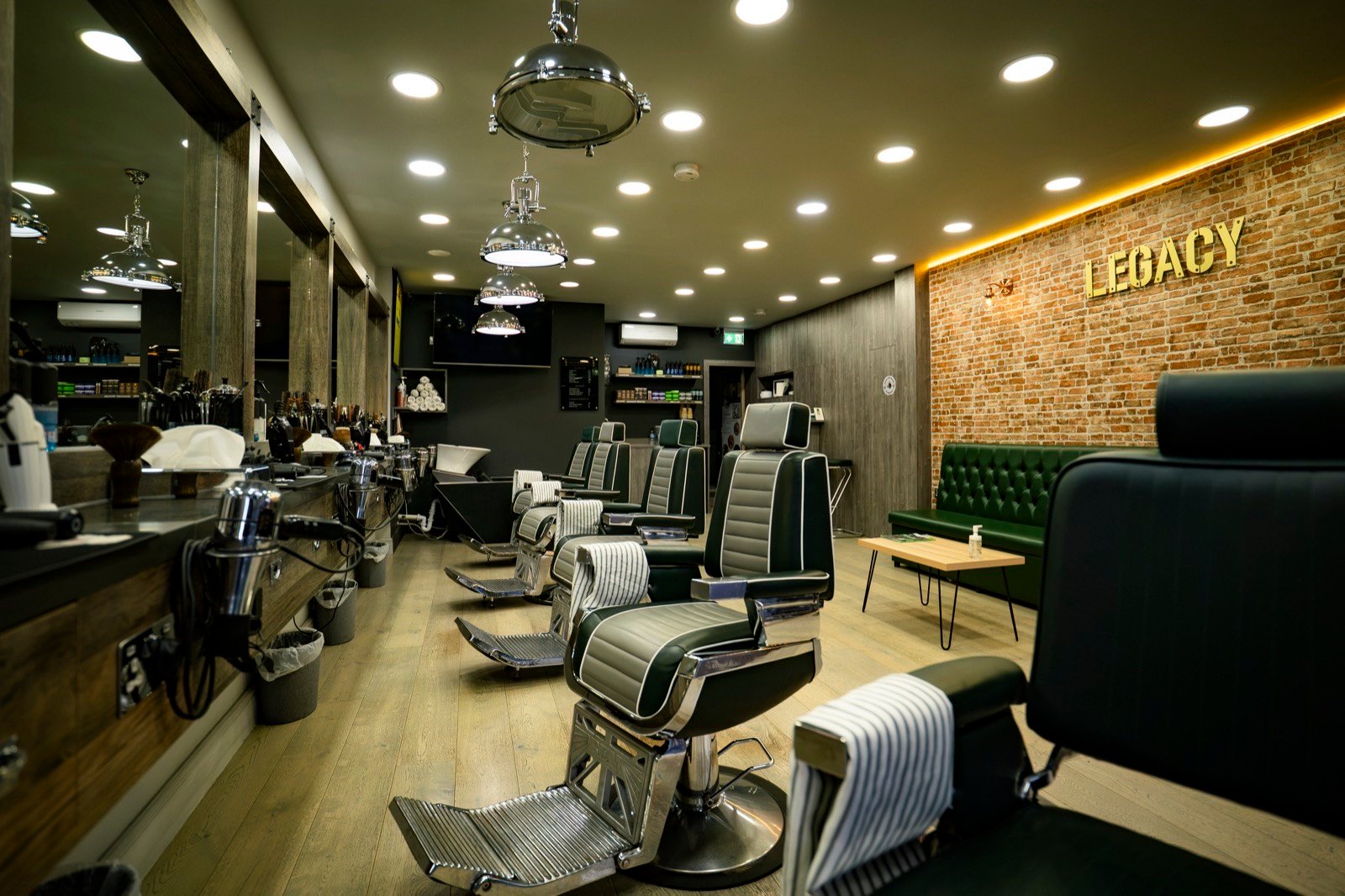 A barbershop with leather chairs, wood panelling and a gold Legacy sign on brick