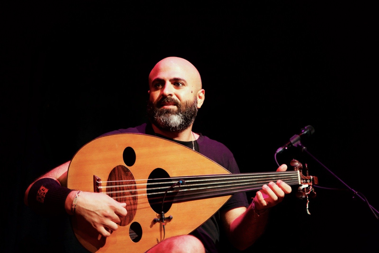 An oud player smiling as he plays, against black