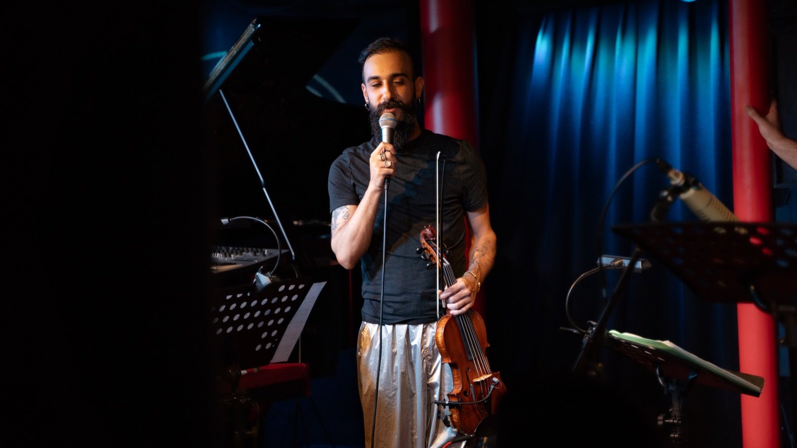 Singing, violin in hand, in front of the blue curtain