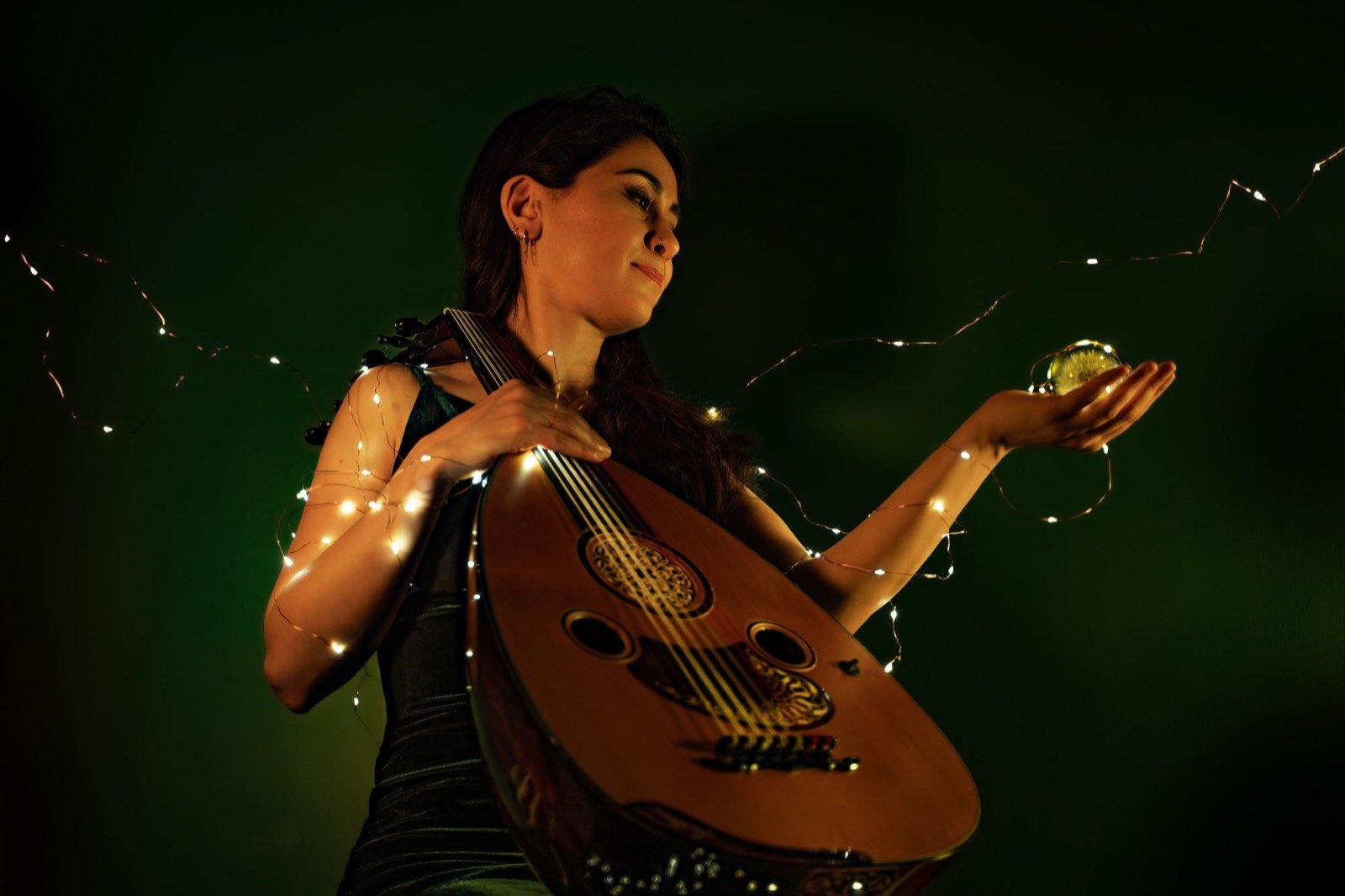 An oud player holding a small glowing globe, wrapped in fairy lights against deep green