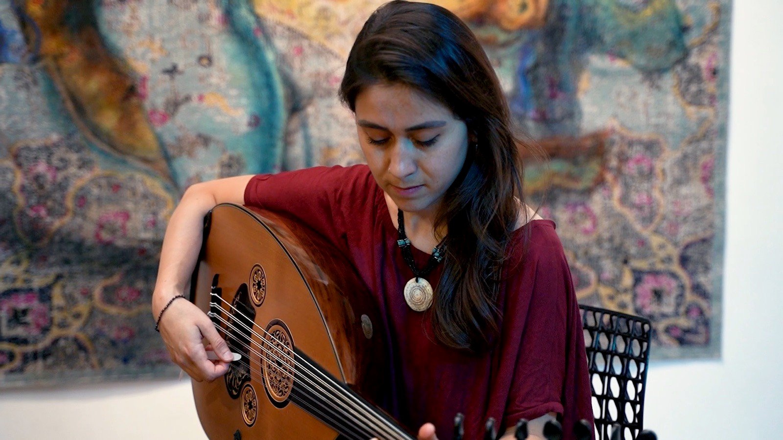 An oud player in red playing in front of a large, bright abstract painting