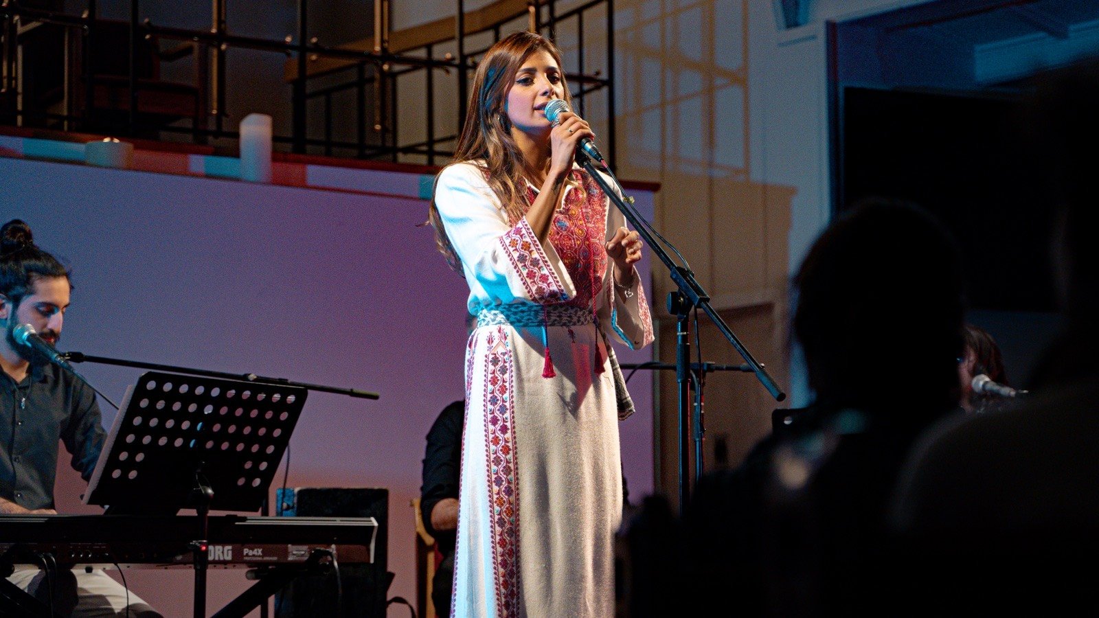 A singer in an embroidered dress at the microphone, the band around her