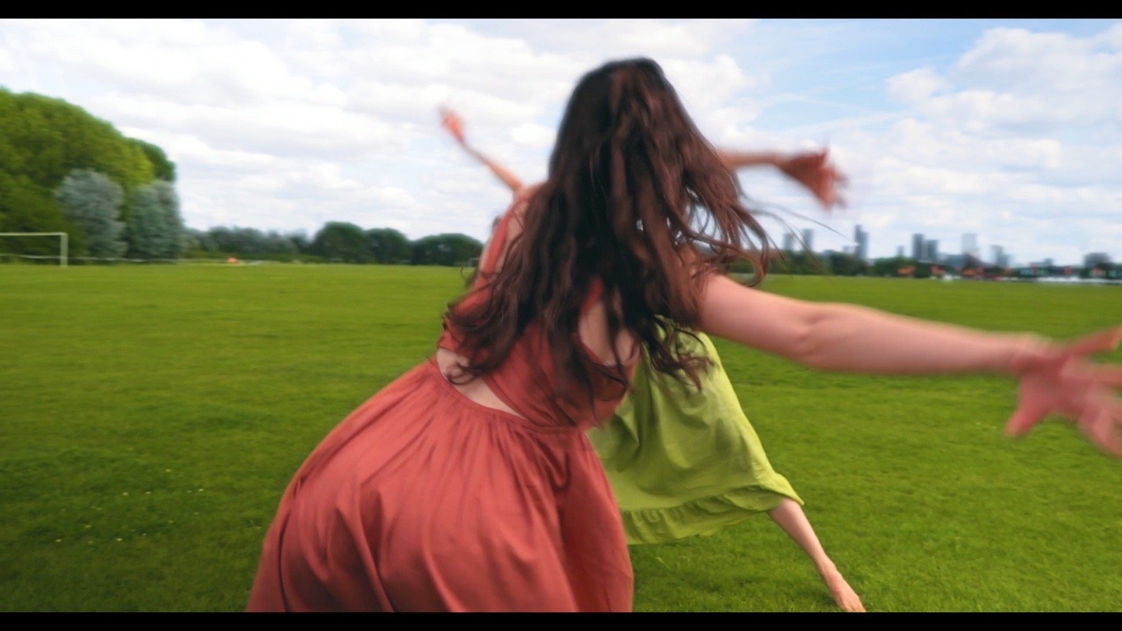 Two dancers in red and green dresses leaping on a sunlit lawn