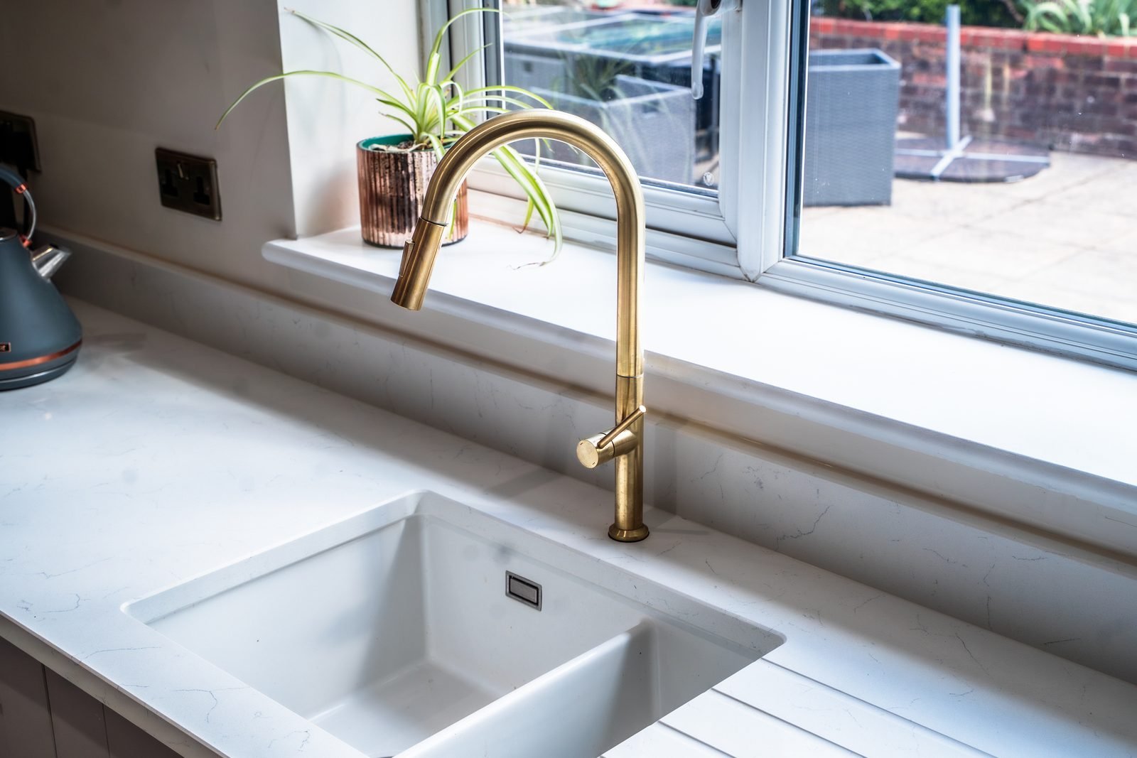 A brass tap over a white sink by the window