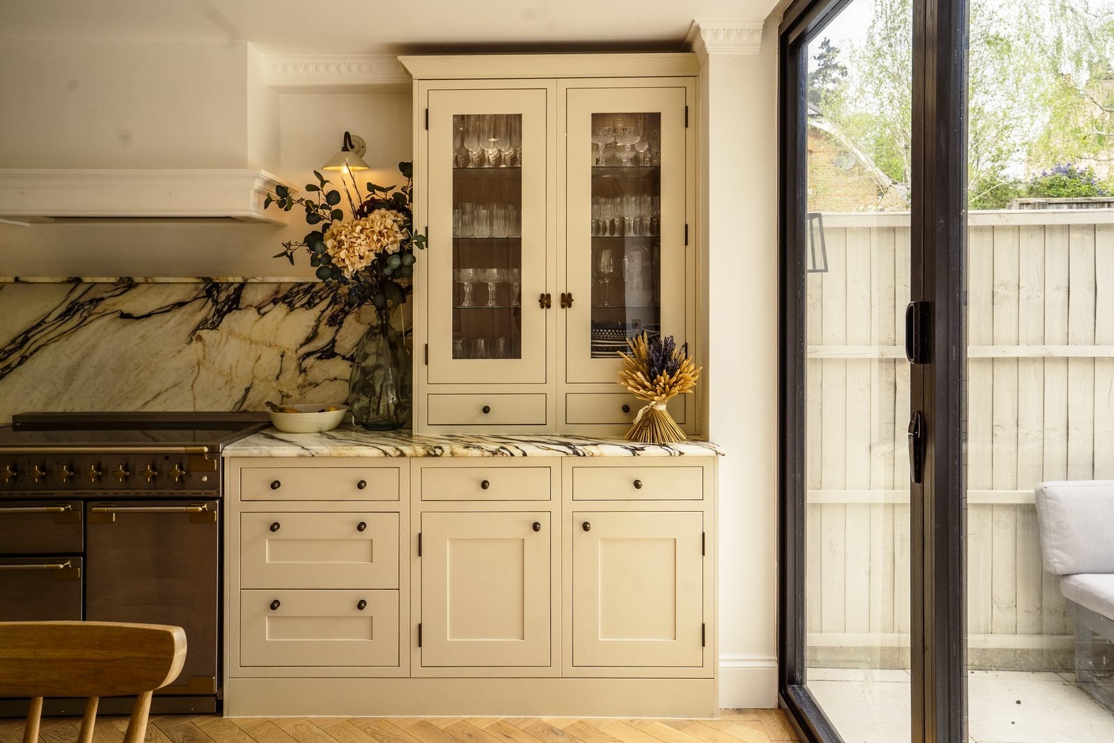 A cream dresser with glass doors beside a range cooker