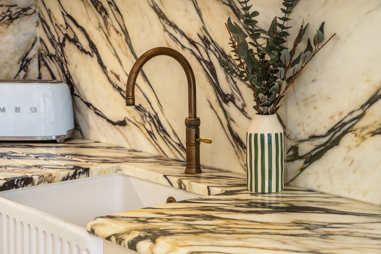 A brass tap over a marble worktop with dark veins