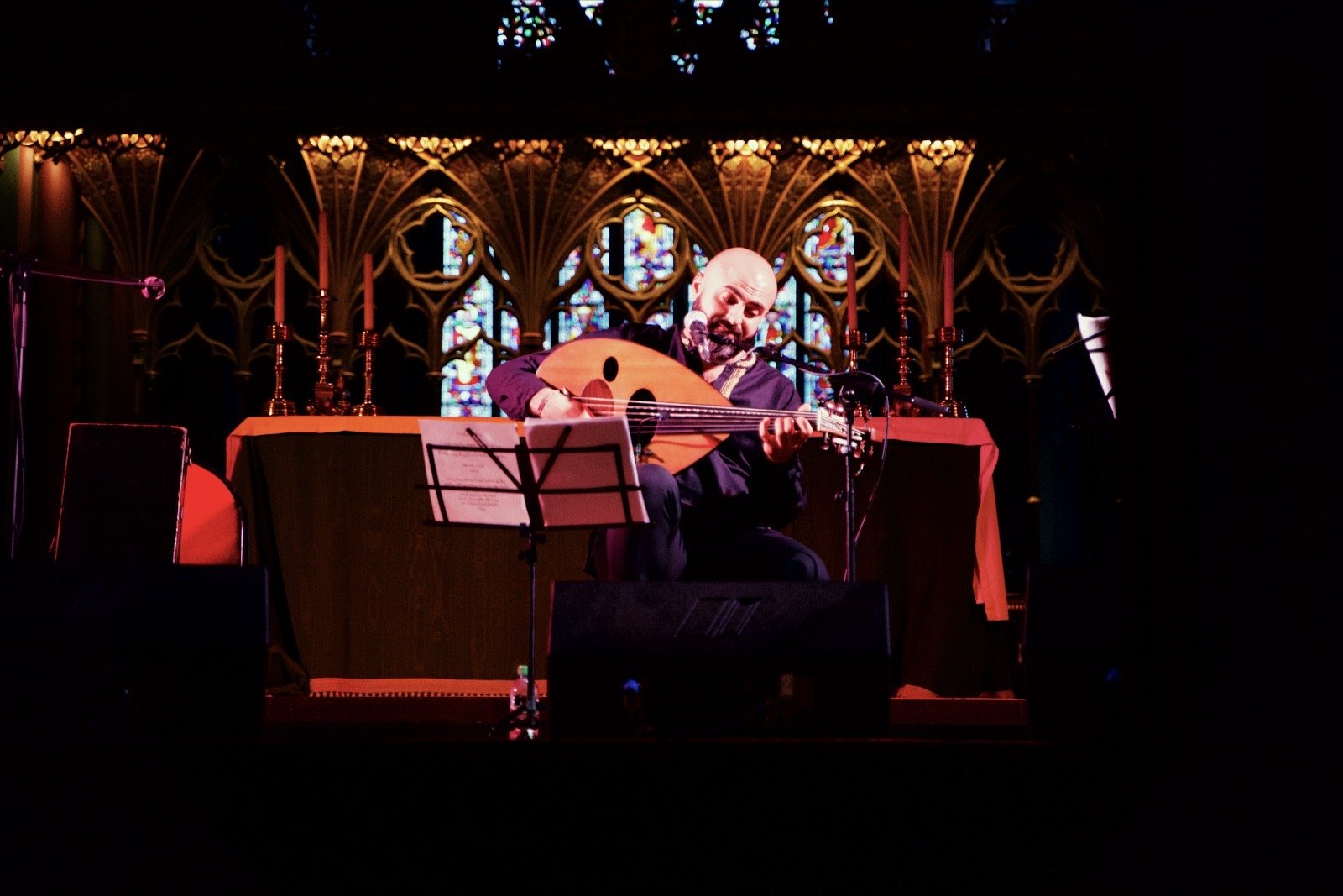An oud player alone in front of the altar and stained glass of a church, lit red