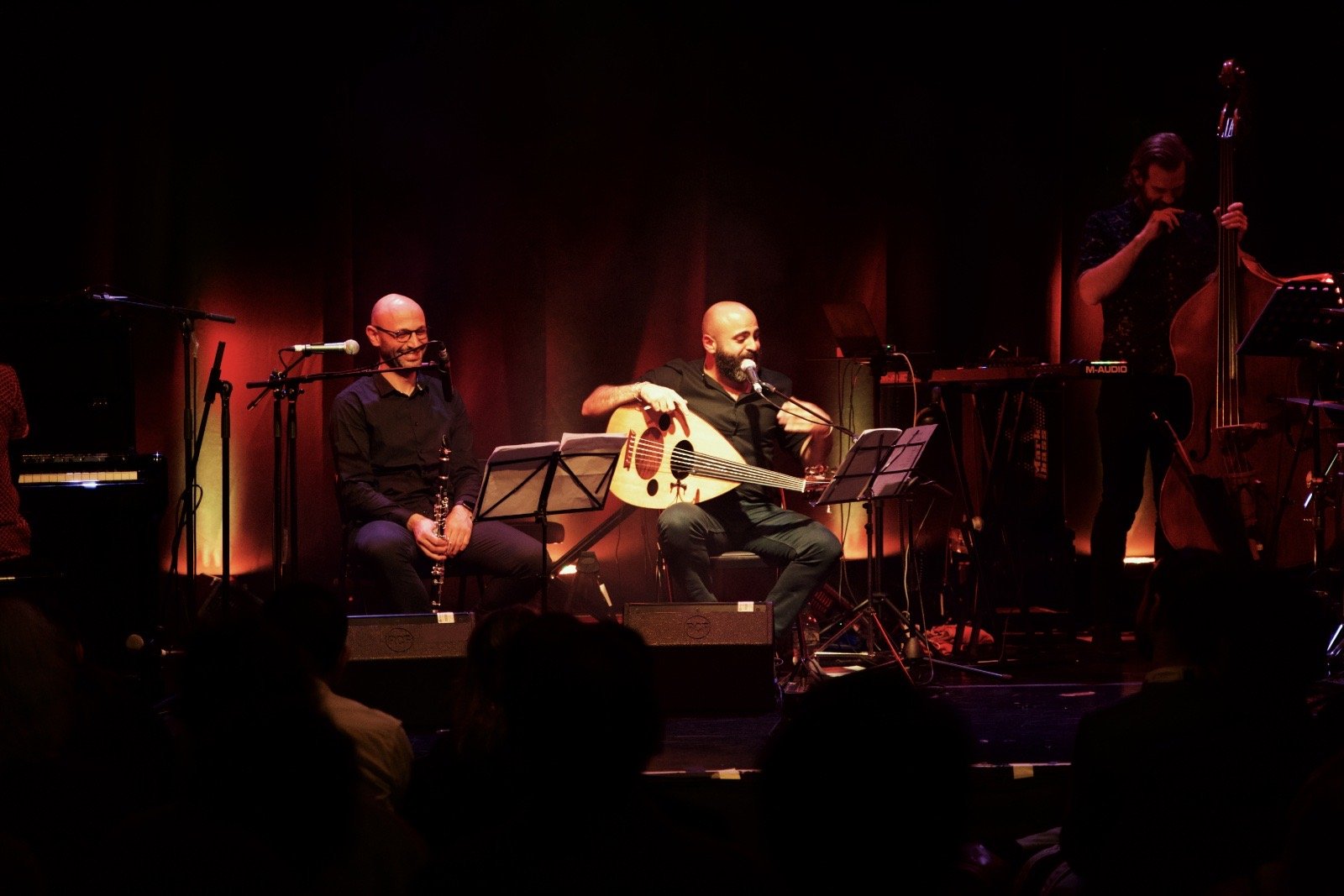 A band on a stage lit red, the audience in silhouette in front