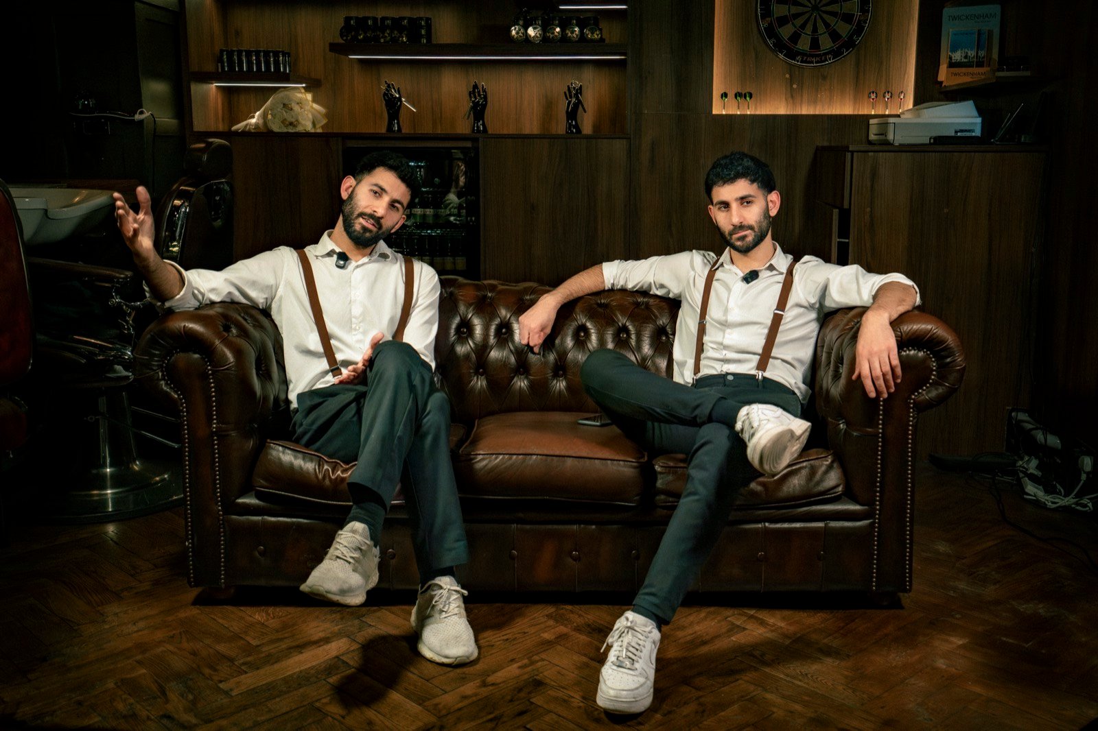 Two barbers sitting on a leather Chesterfield in their shop