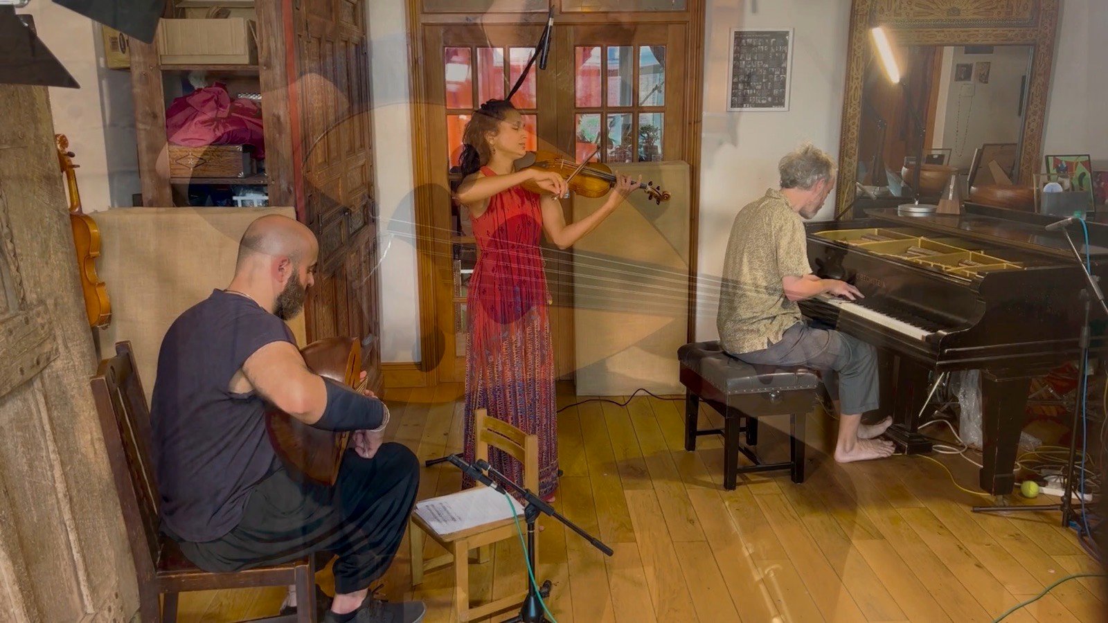 A violinist in red, an oud player and a pianist playing together in a wood-panelled room